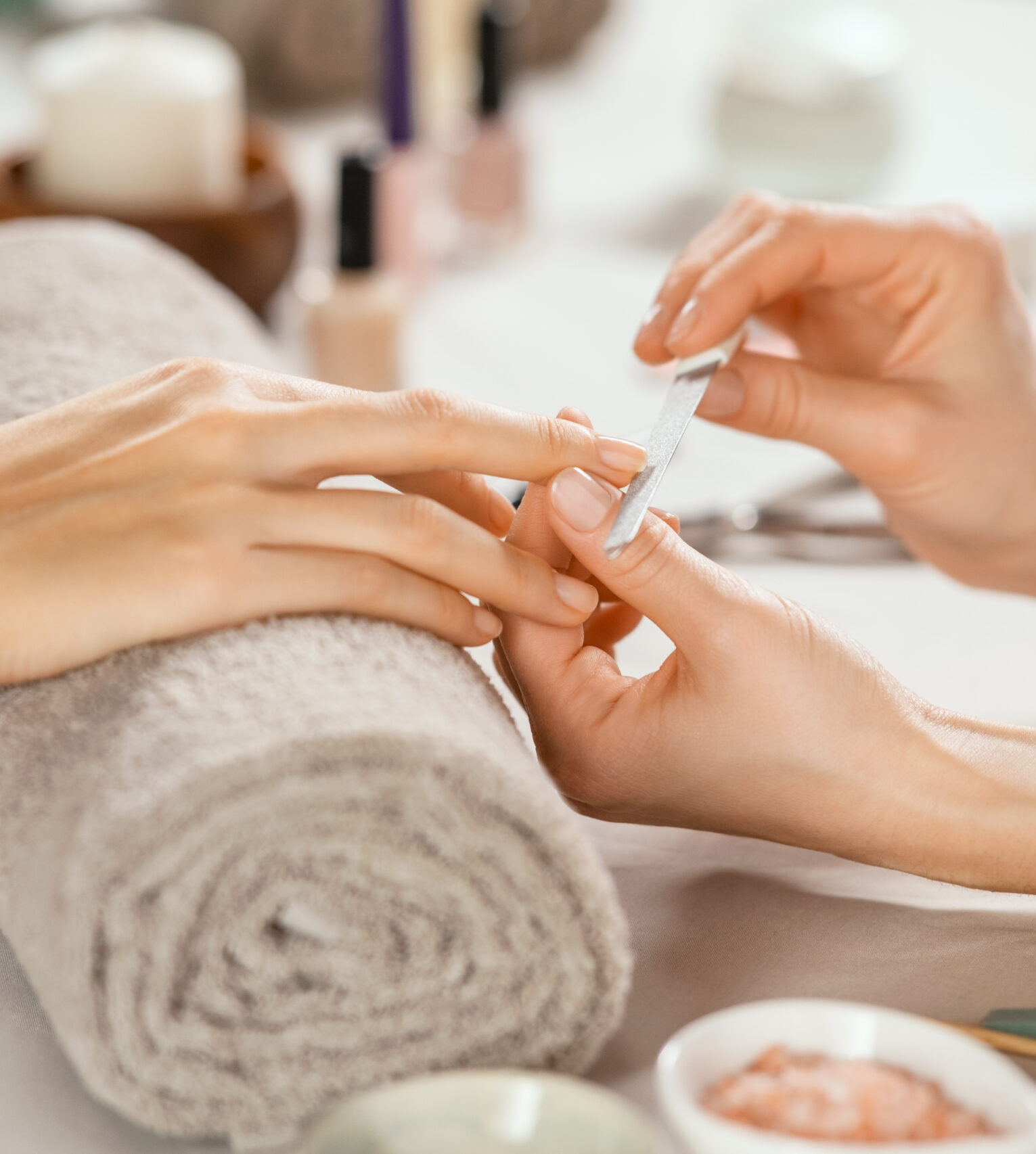 Close up shot of a woman in a nail salon receiving manicure by beautician with metal nail file. Woman getting nail manicure at spa centre. Beautician file nails to a customer in luxury salon.